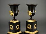 pair of black and gold vases with handles on pedestals