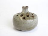 a small gray vase with holes in it on a white surface