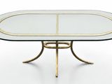 une table à manger ovale en verre avec des pieds en métal doré et un plateau en verre