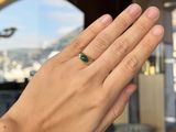 a woman ' s hand holding a ring with a green stone on it