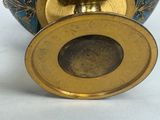 a blue and gold vase with a gold lid on a table