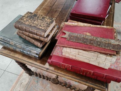 Plusieurs vieux livres sont empilés sur une table en bois, à côté d'une chaise rouge.