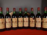 six bottles of red wine lined up on a red table