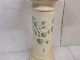 a white vase with green leaves on it sitting on a table