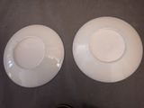 two white plates sitting on a table with a person standing next to them