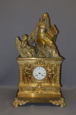 une horloge en or surmontée d'une statue représentant une femme tenant un livre