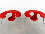 two red chairs sitting on top of a cement floor next to each other