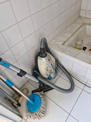 un aspirateur et un balai dans une salle de bains, à côté d'une baignoire