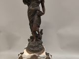 statue of a woman holding a bird on a marble base with a clock in the foreground