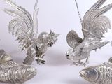 trois figurines en métal argenté représentant des oiseaux et des poissons, posées sur une surface blanche