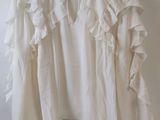 white blouse with ruffles hanging on a hanger against a white wall