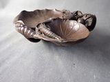 a metal bowl with a leaf on it on a table