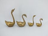 three brass swan figurines sitting side by side on a white surface