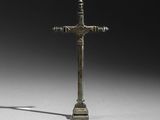 une image représentant une croix en bronze posée sur un socle, avec une ombre projetée au sol