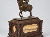une statue en bronze représentant un homme à cheval, posée sur un socle en bois