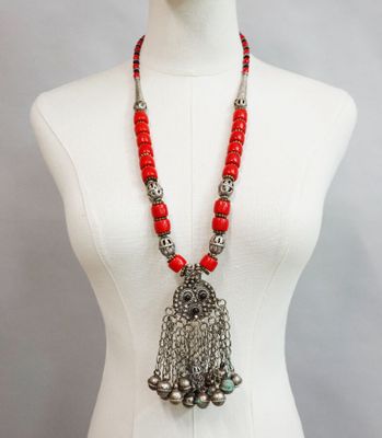 a mannequin torso with a red beaded necklace and silver bells
