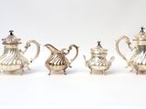 four pieces of silver tea and coffee set on a white surface