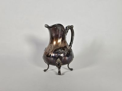 un pichet ancien plaqué argent posé sur un socle, sur fond blanc