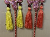 trois bâtons décoratifs ornés de pompons et de perles, posés sur une table