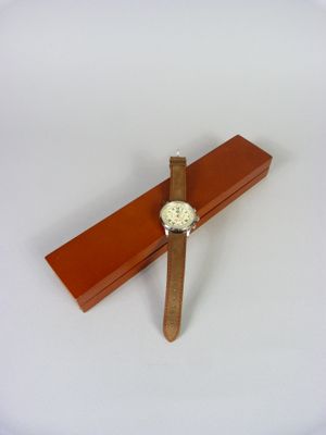 une croix en bois sur laquelle est posée une montre, posée sur une surface blanche
