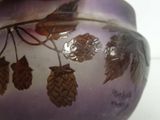 a hand holding a purple vase with leaves painted on it