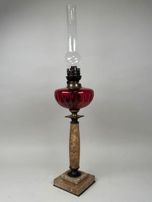 une lampe à huile à l'ancienne, dotée d'un abat-jour en verre rouge et posée sur un socle en bois