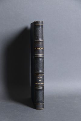 an old black book sitting on top of a table next to a gray wall