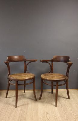 two wooden chairs with wicker seats against a gray wall