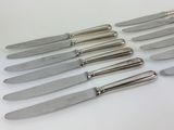 six silverplated knives are lined up on a white surface