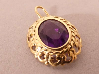 a close up of a gold pendant with a purple stone