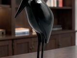 une statue représentant un oiseau noir, posée sur une table devant une bibliothèque