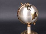 a silver and gold globe on a stand on a black surface