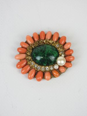 un gros plan sur une broche ornée de perles et d'une pierre verte
