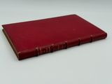 an old red book sitting on top of a white table