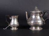a silver tea pot and a silver cup on a table