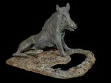 statue of a wild boar sitting on a rock with a black background