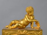 a gold statue of a baby laying on top of a clock