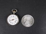 une vieille montre de poche posée à côté d'une pièce de 25 cents