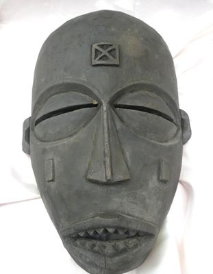 un masque noir orné d'une croix, posé sur un drap blanc