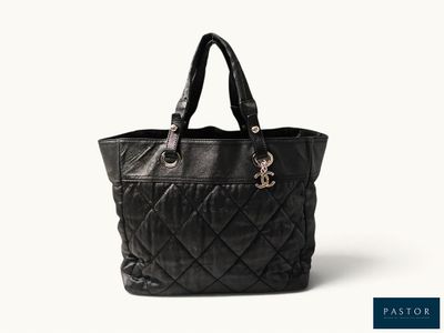 un sac fourre-tout noir matelassé posé sur une surface blanche