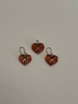 une paire de boucles d'oreilles en forme de cœur, de couleur cuivrée, posées sur un fond blanc