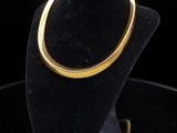 a gold necklace on a black mannequin stand against a black background