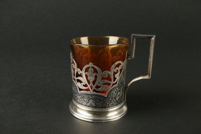 une tasse en argent et en verre munie d'une anse, posée sur une surface noire