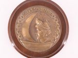 une médaille d'or sur laquelle est représenté un voilier, sur un fond blanc