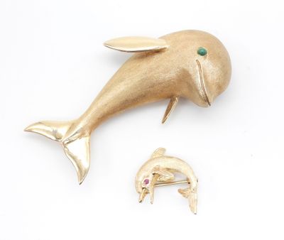 une broche en forme de dauphin en or, avec une pierre verte dans la bouche