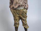 statue en bronze représentant un garçon portant un chapeau et une chemise, posée sur un socle noir