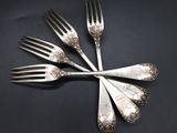 four forks are arranged in a circle on a black surface