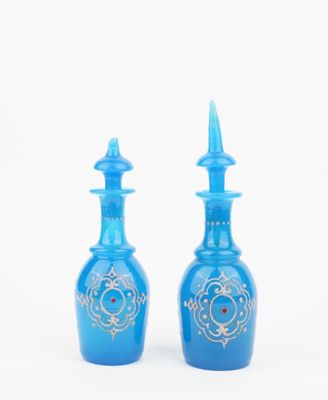 two blue glass bottles with gold designs on them on a white background