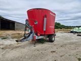 a red tractor trailer parked in a dirt lot next to a barn