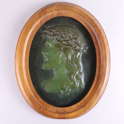 une sculpture ovale représentant la tête d'une femme, dans un cadre en bois